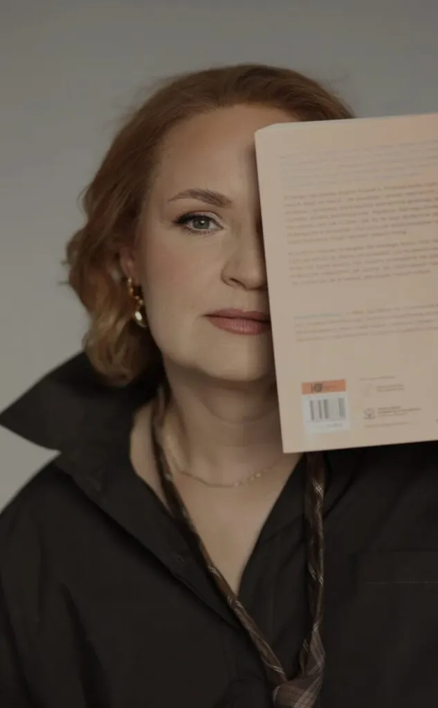 Alina Chodzicka, fundatorka Fundacji Centrum Feedbacku, zasłaniająca połowę twarzy otwartą książką